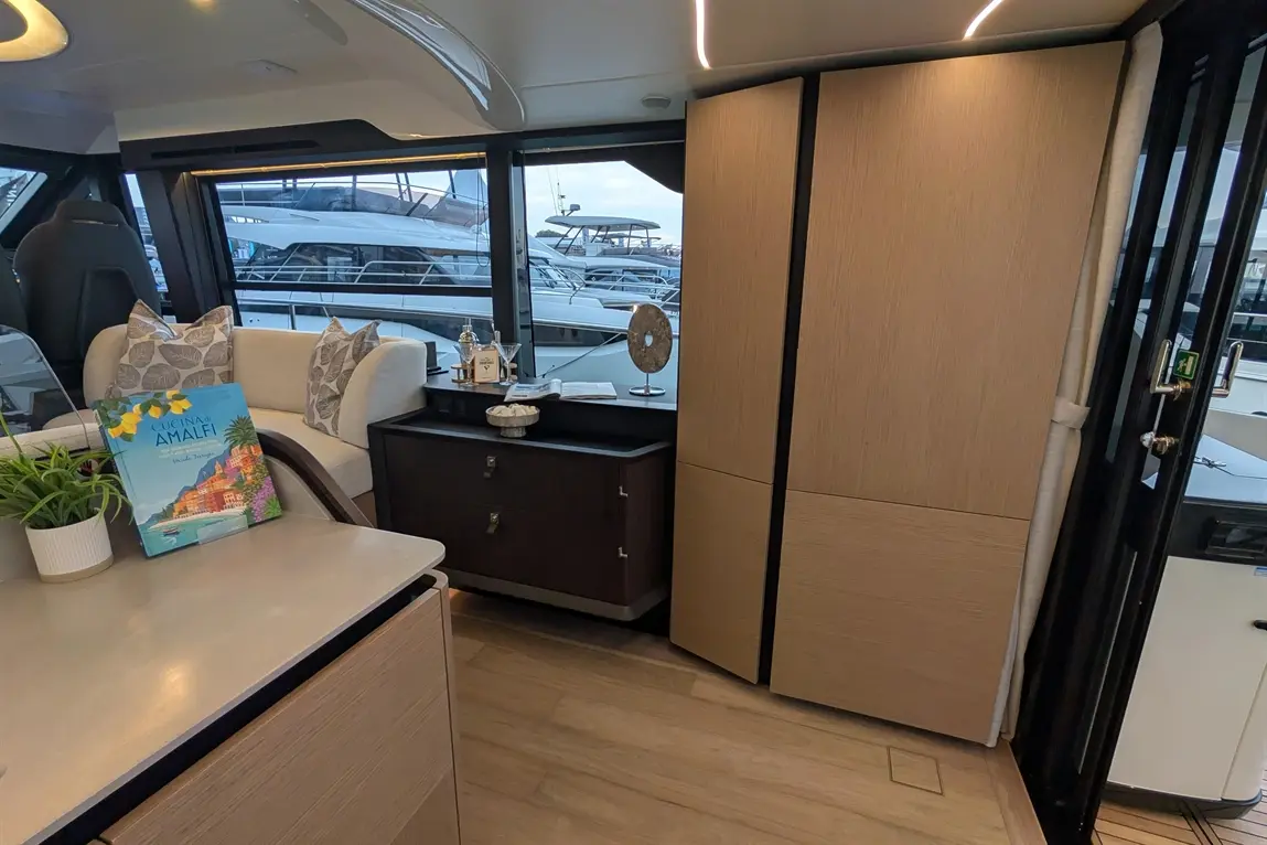 Stylish boat interior featuring a seating area, a book titled "Cucina di Amalfi," and views of moored yachts through windows.